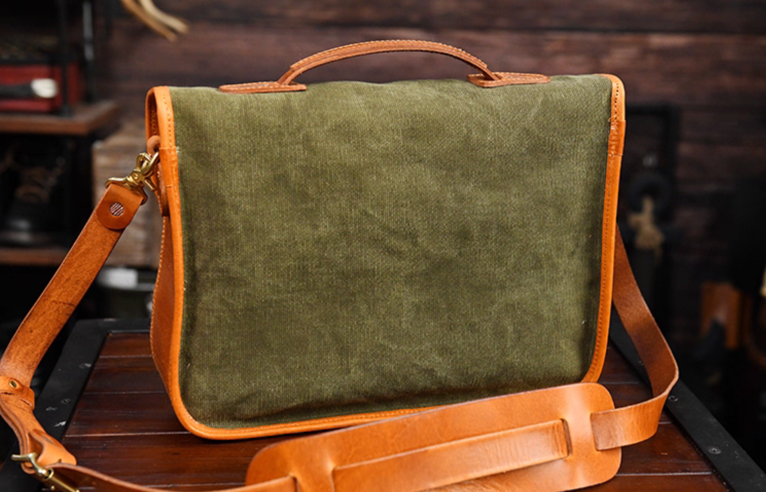 Back view of green waxed canvas satchel with leather handle and trim