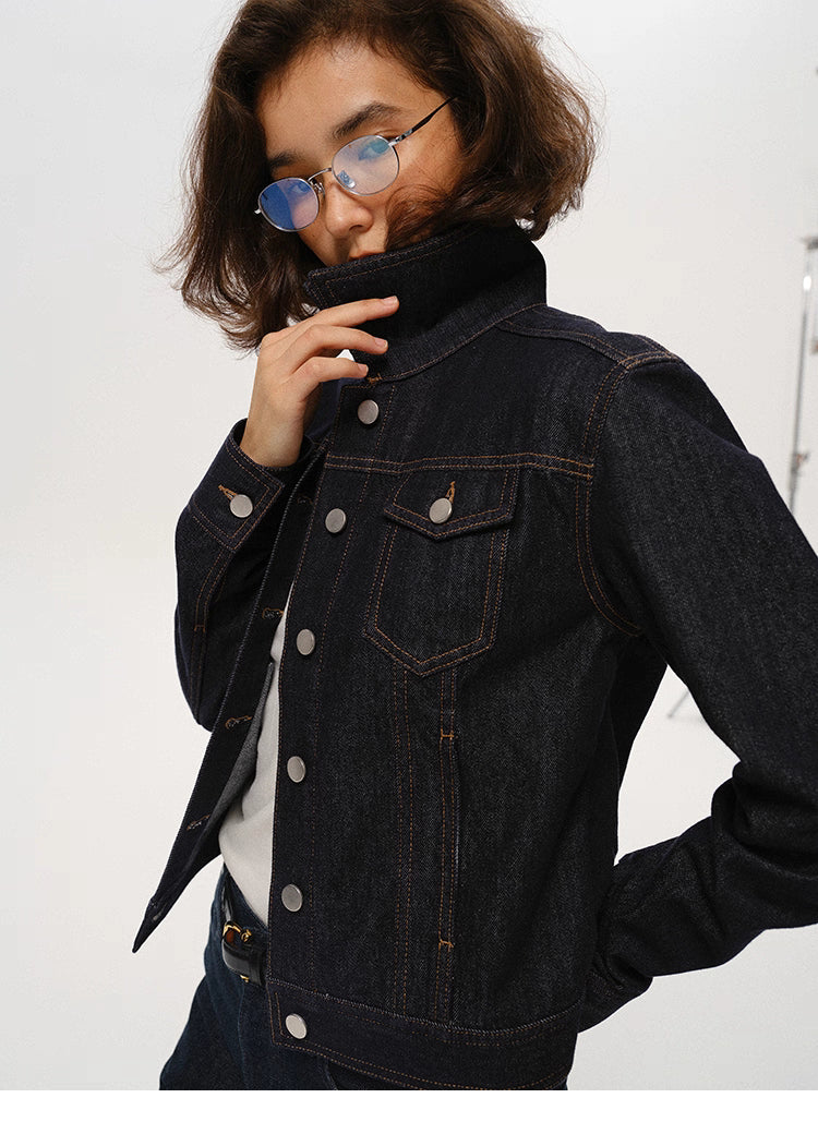 woman lifting high collar of dark indigo denim jacket wearing blue-tint glasses