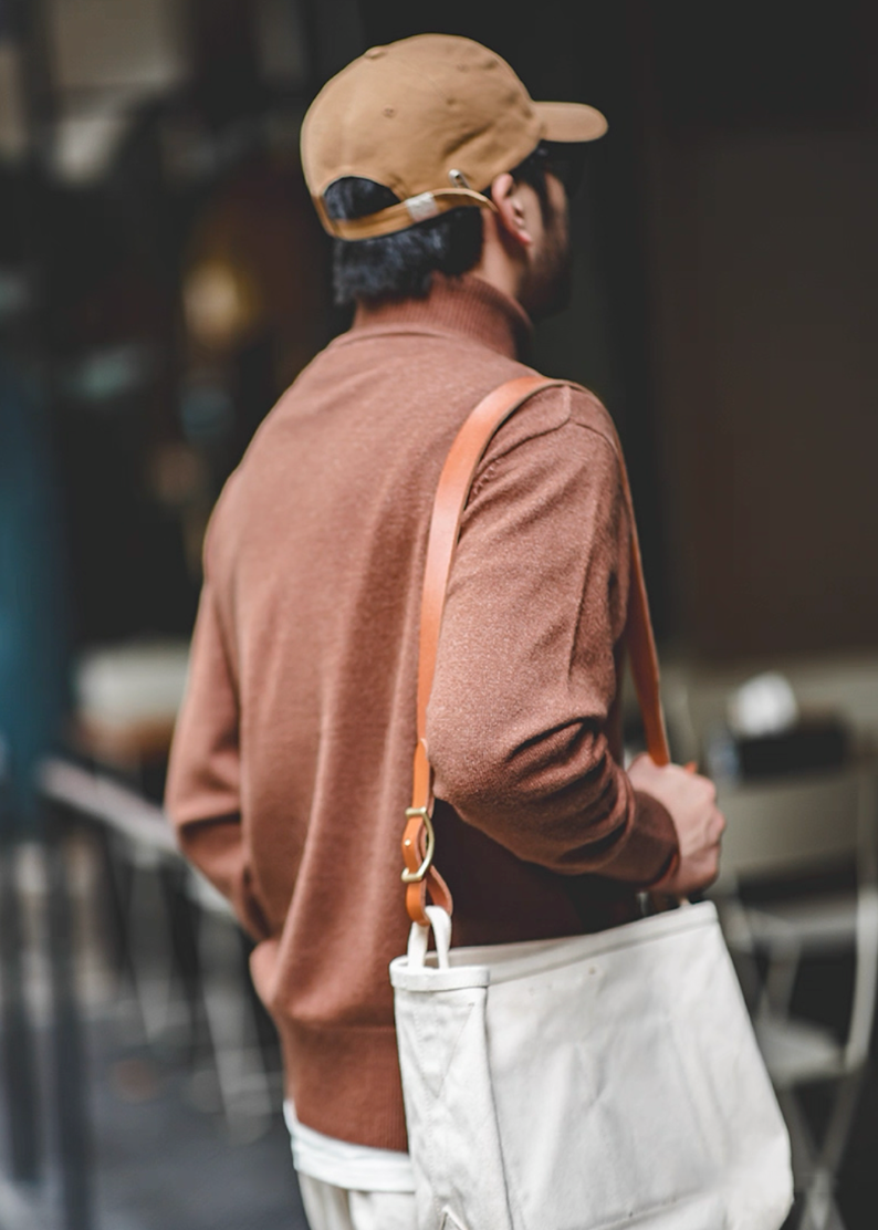 Back view of man wearing mocha brown turtleneck with tan leather-strap tote bag
