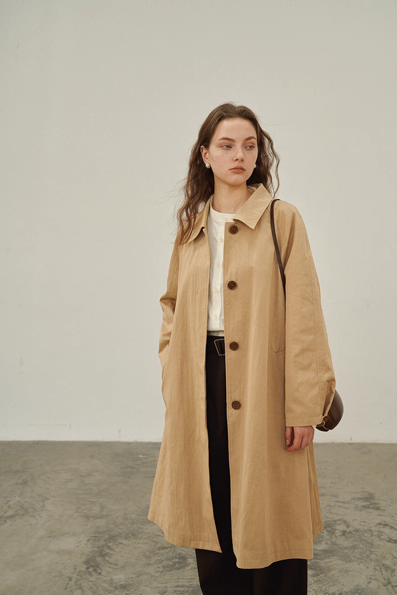Model wearing beige khaki A-line raglan trench coat styled with dark trousers.