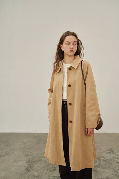 Model wearing beige khaki A-line raglan trench coat styled with dark trousers.