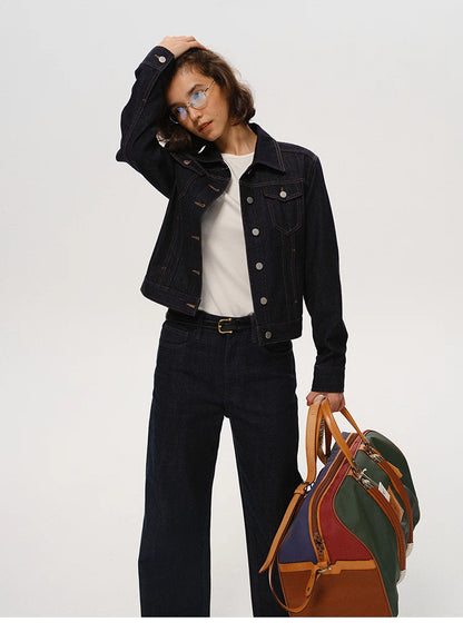 full-body shot of woman in dark indigo denim jacket holding a travel bag