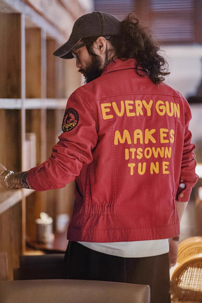 Back view showing yellow chain-stitch text “Every Gun Makes Its Own Tune”