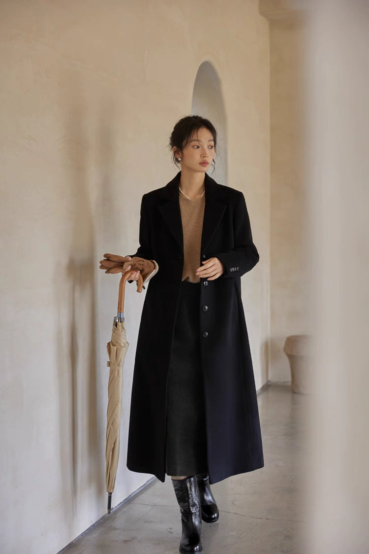 Woman in a black wool long coat styled with a beige sweater and knee-high boots, holding an umbrella.