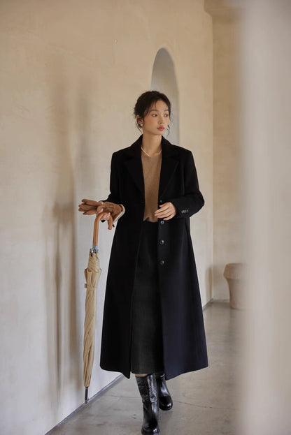 Woman in a black wool long coat styled with a beige sweater and knee-high boots, holding an umbrella.