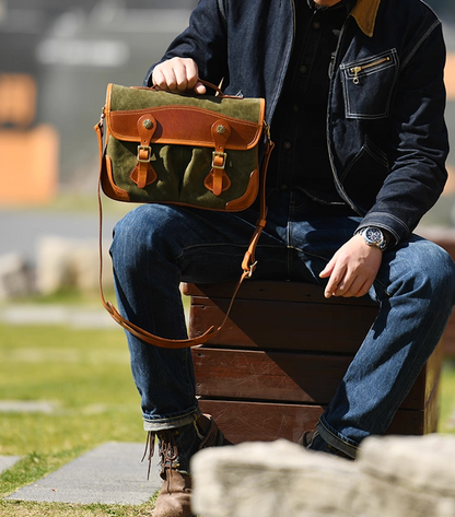Man holding olive waxed canvas satchel in outdoor urban setting wearing denim jacket