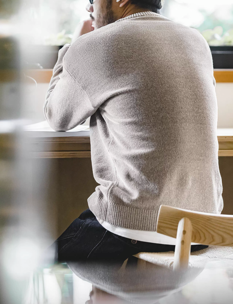 Back view of man sitting by the window wearing light gray chenille sweater