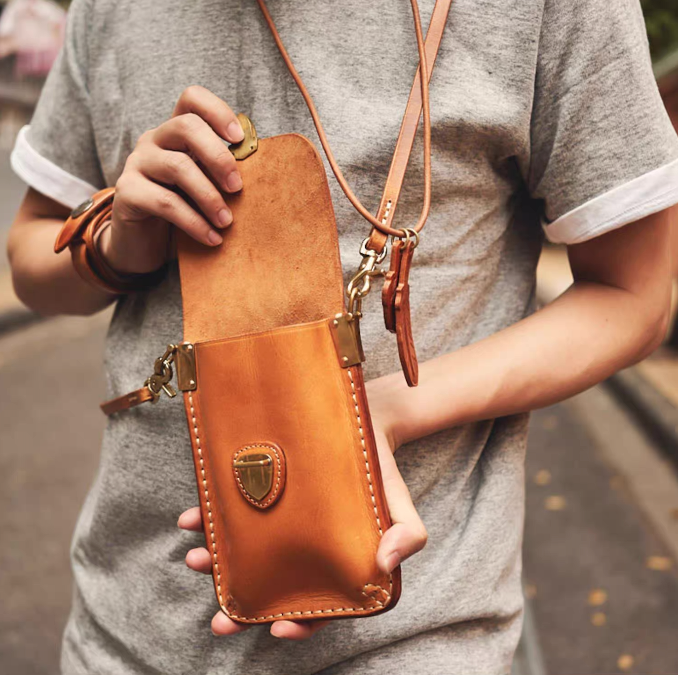 Model carrying amber brown leather crossbody pouch with flap open on city street.