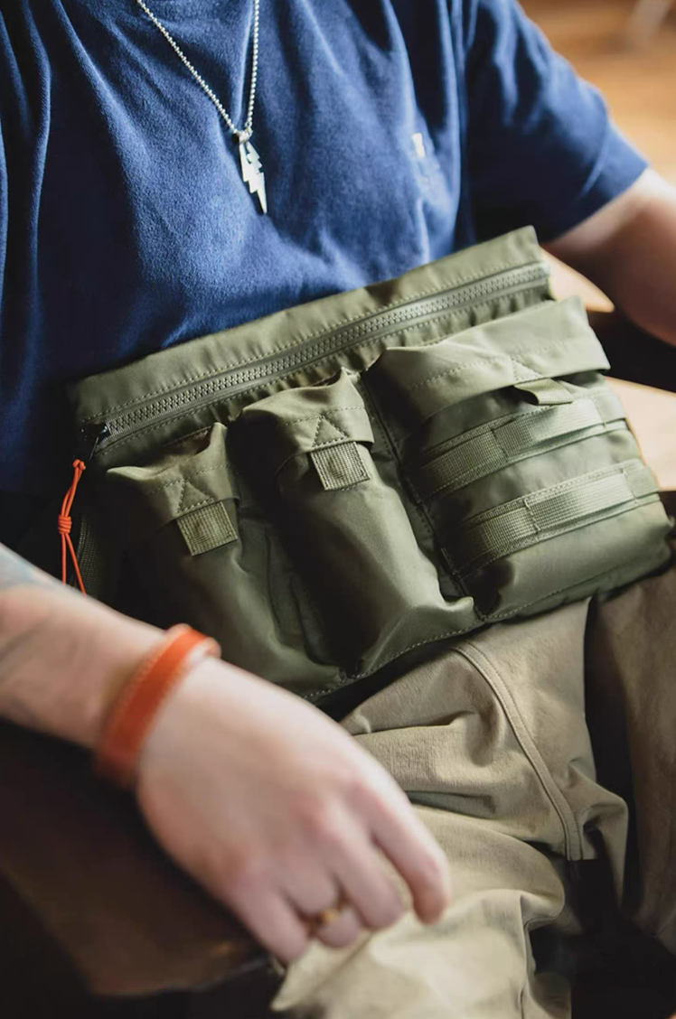 Man wearing army green crossbody bag over navy tee, highlighting front cargo pouches