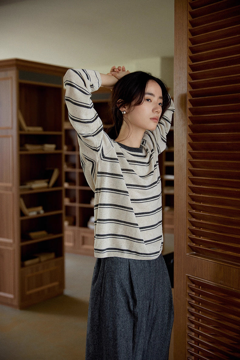 Woman stretching arms wearing oat and dark gray striped Tencel-linen pullover, showing soft drape.
