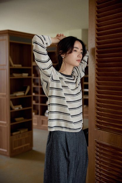 Woman stretching arms wearing oat and dark gray striped Tencel-linen pullover, showing soft drape.