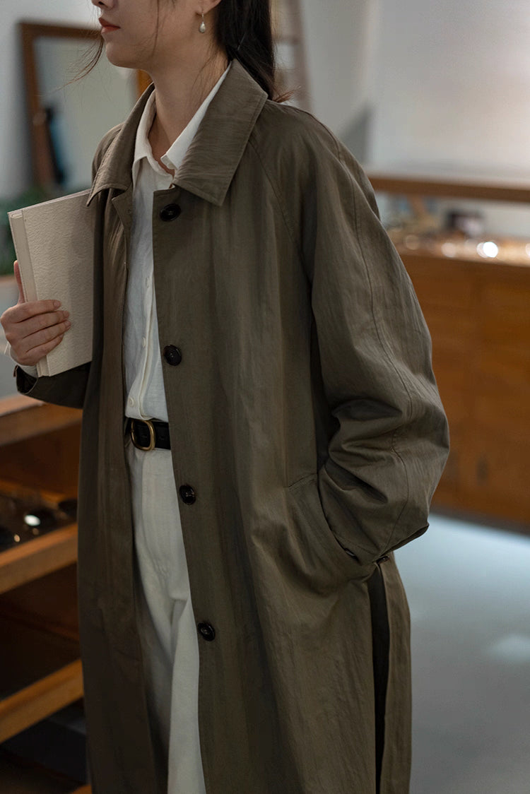 Olive gray-green A-line coat worn indoors with white shirt styling.