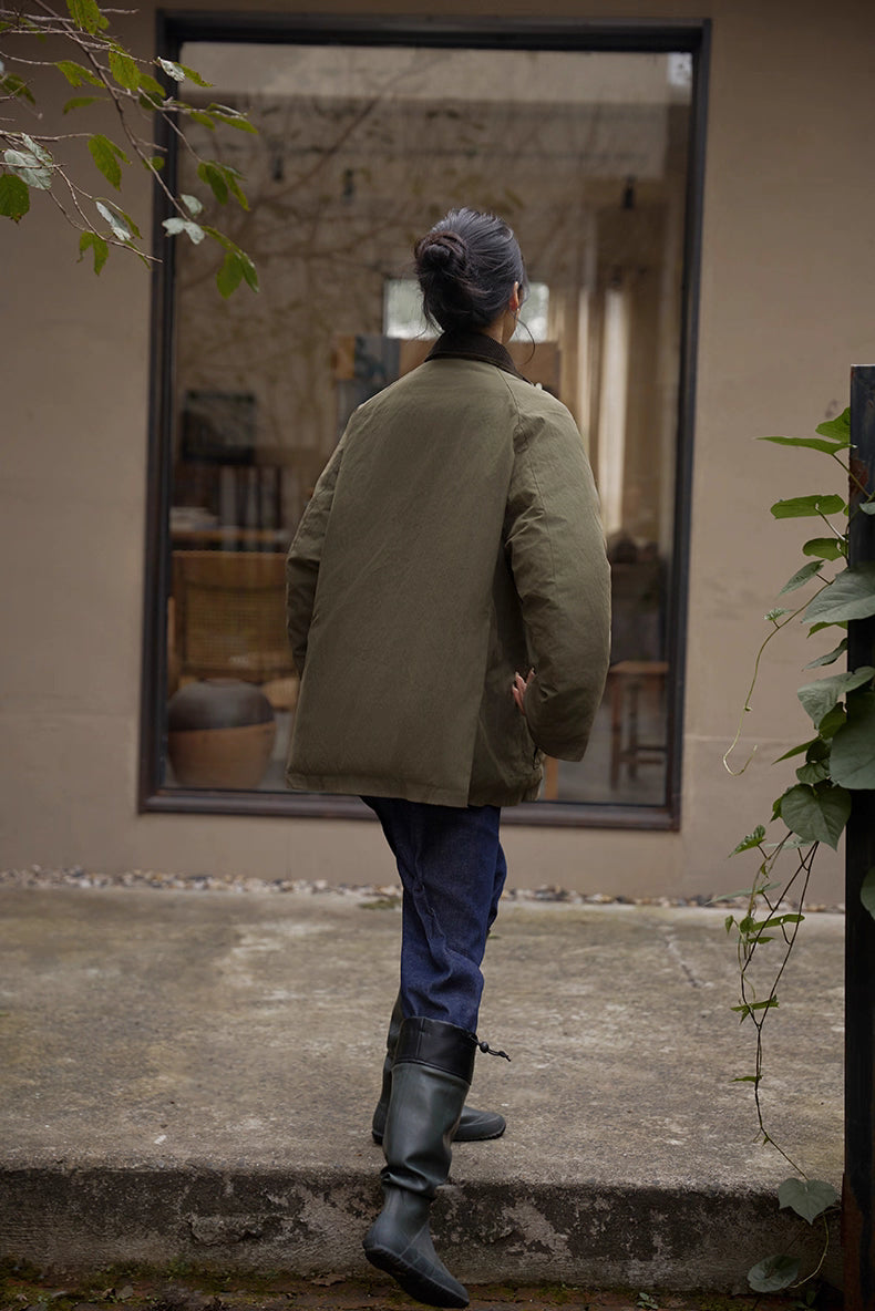 Back view of army green outdoor down jacket as model walks toward doorway.