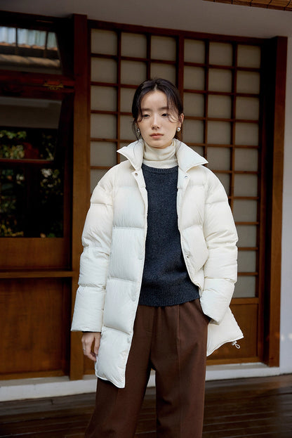 Front view of off white Cloud-Contour Down Coat on porch, styled with turtleneck and brown trousers