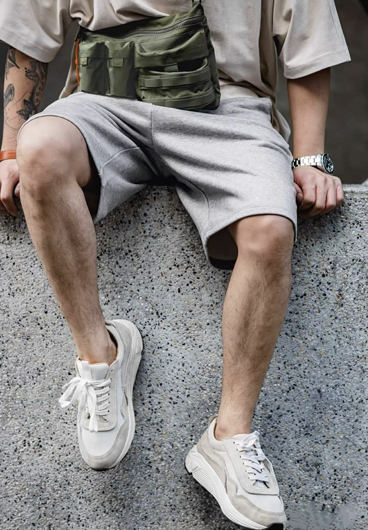 Man sitting outdoors wearing army green utility bag styled with grey shorts