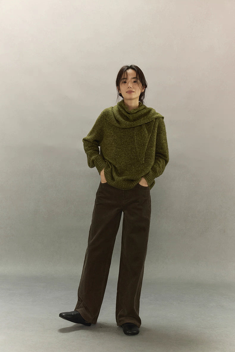 Woman standing with hands in pockets wearing moss green cashmere sweater, calm minimal look.