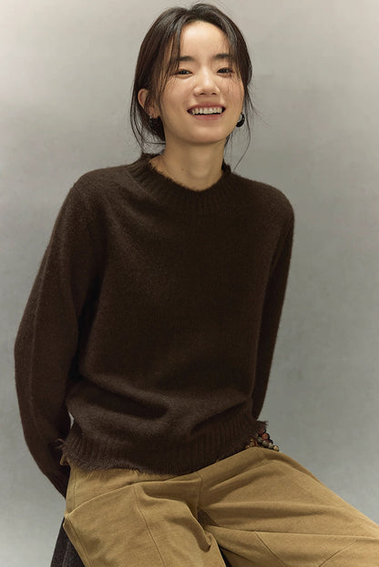 Seated view of model in dark coffee brown yak wool sweater paired with tan pants.
