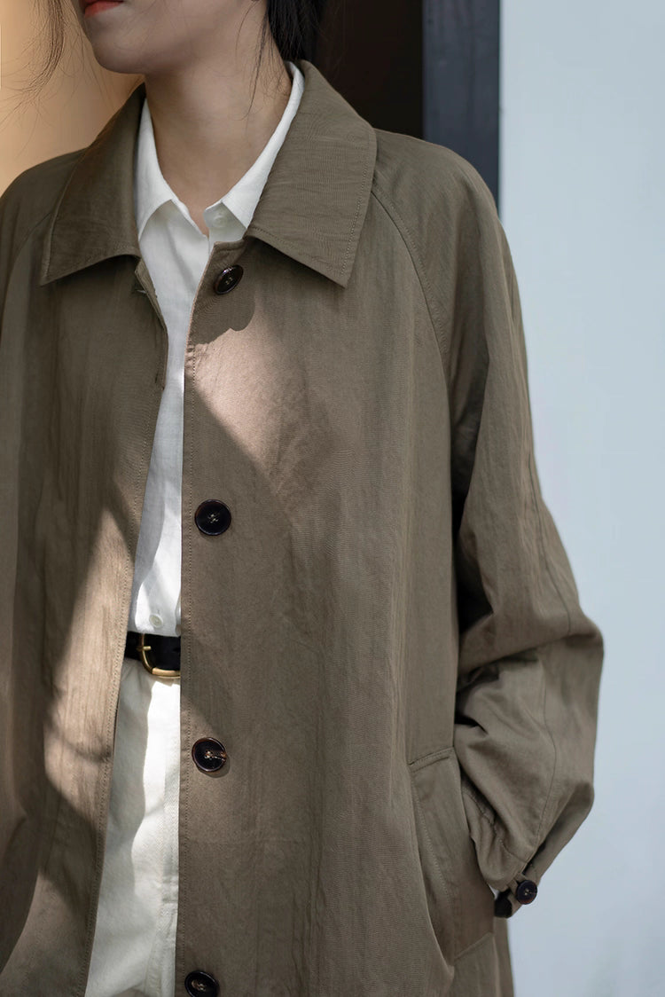 Close-up of button front and textured fabric of olive gray-green trench coat.