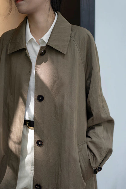 Close-up of button front and textured fabric of olive gray-green trench coat.
