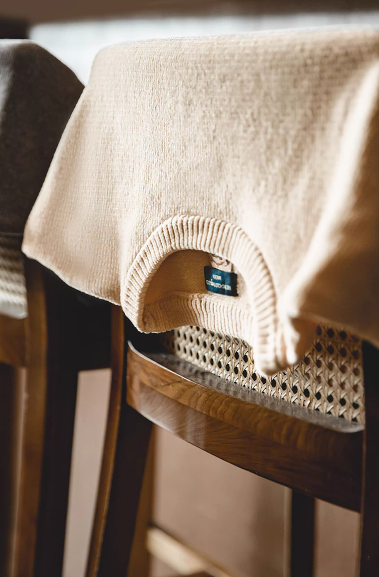 Cream chenille sweater draped over wooden chair highlighting knit detail