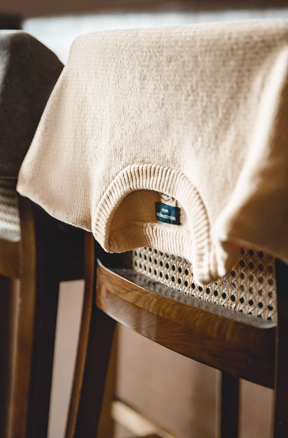Cream chenille sweater draped over wooden chair highlighting knit detail