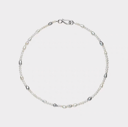 Elegant baroque pearl choker flat lay featuring irregular freshwater pearls in white and soft gray tones arranged on a minimalist silver chain