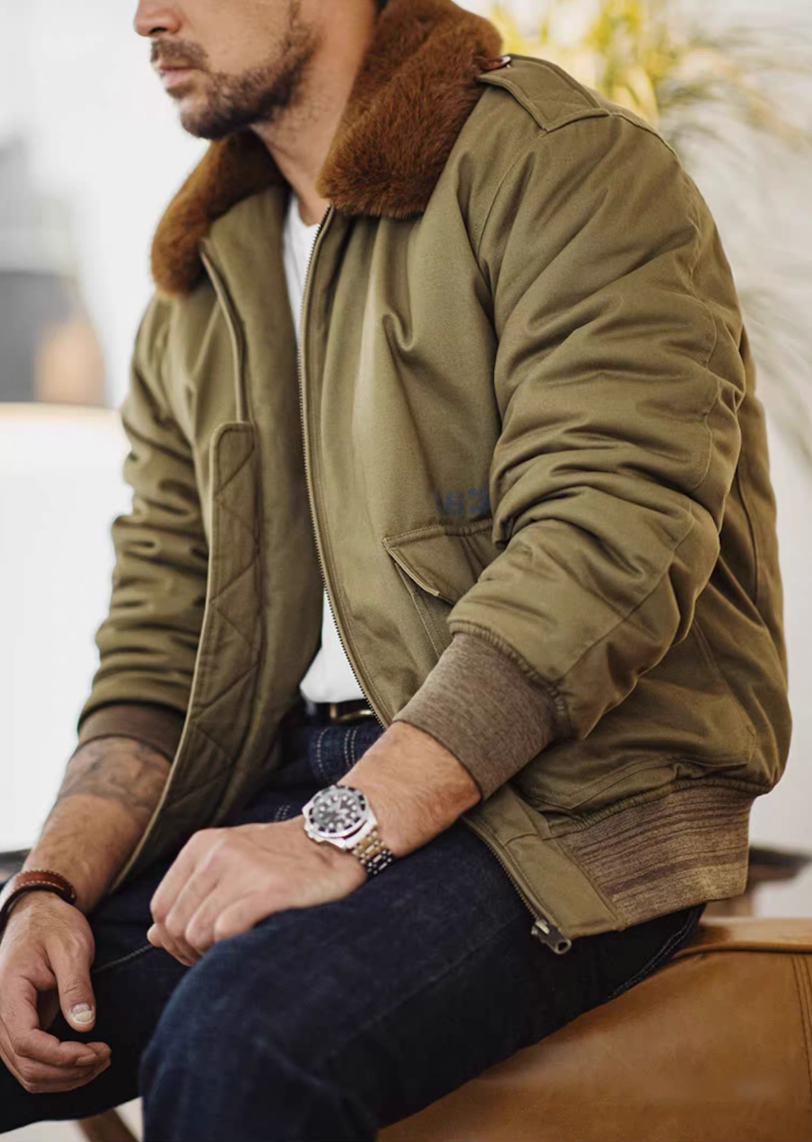 Man seated wearing B-10 cotton bomber with faux-fur collar and dark jeans in casual pose.