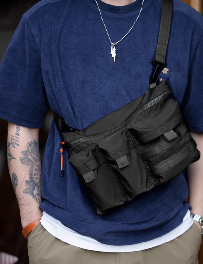Man wearing black crossbody bag with navy tee and khaki pants in urban environment