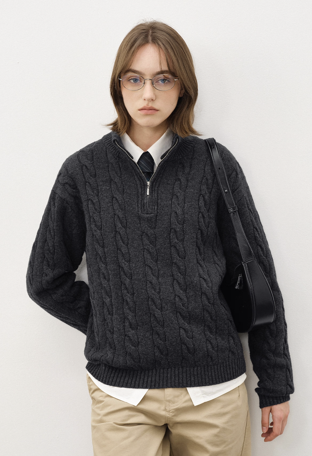 Model wearing dark grey half-zip cable knit sweater with tie and beige pants, smart casual look