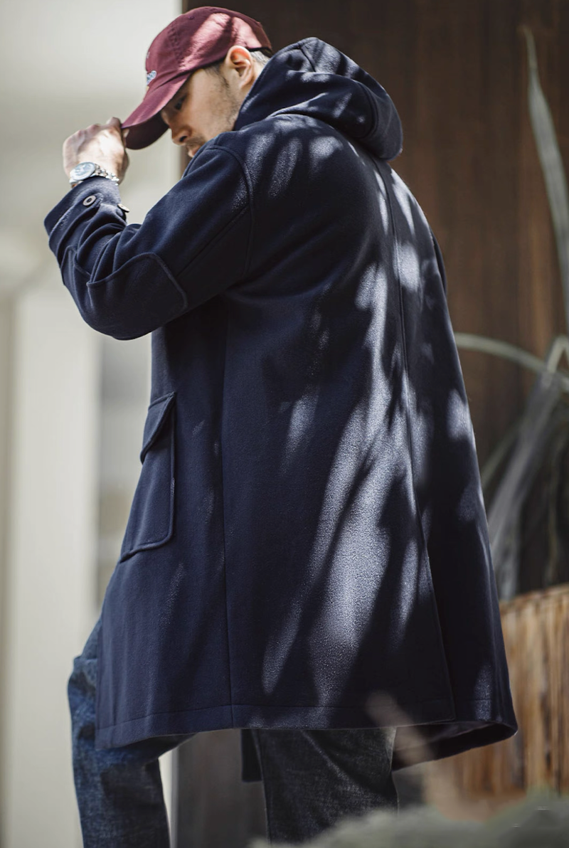 Back view of man wearing navy duffle coat and red cap under sunlight