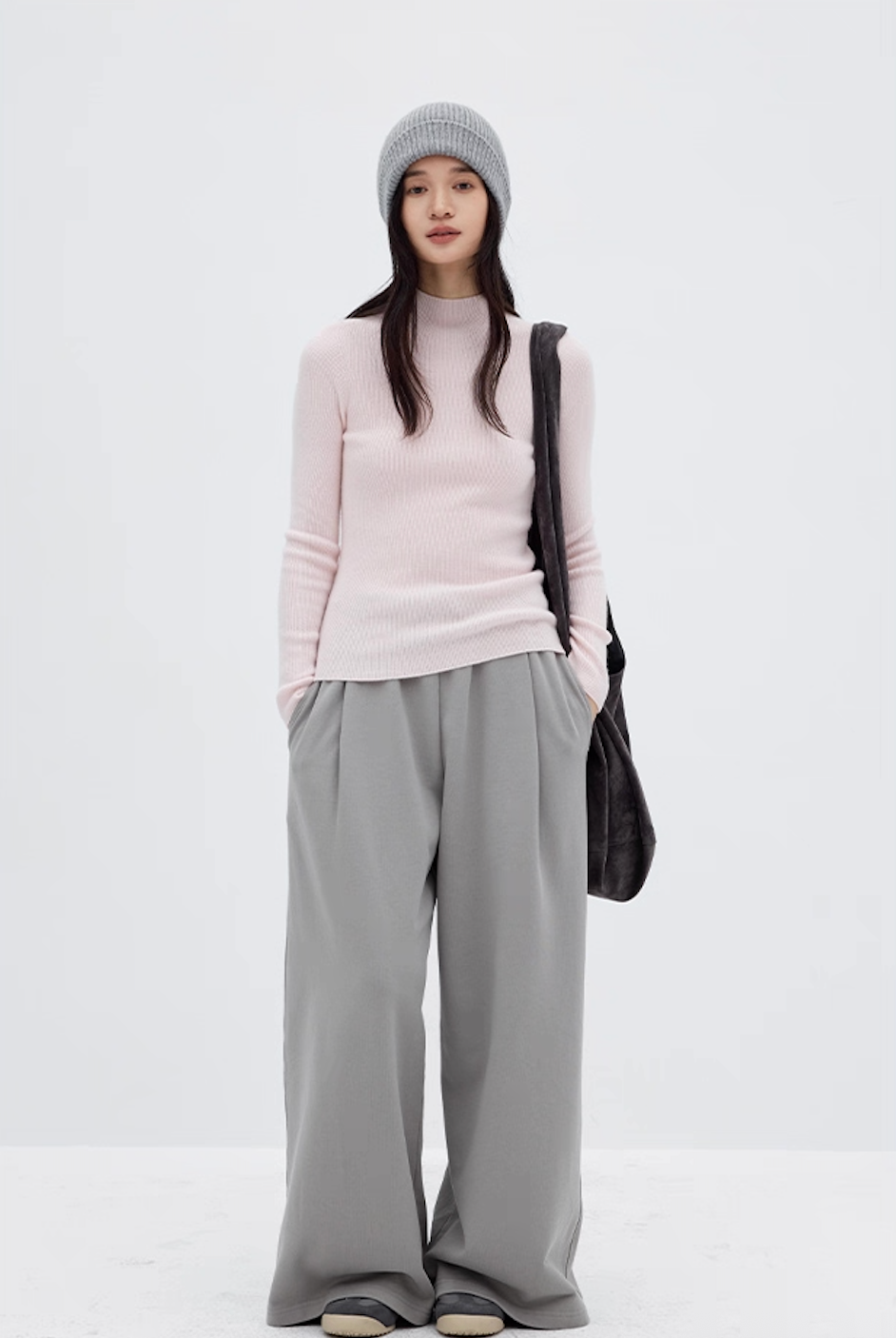 Model wearing light pink cashmere mock neck sweater with gray wide-leg pants and gray beanie, minimalist winter outfit