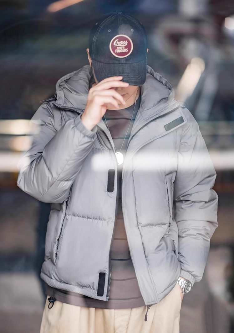 Close-up of model wearing grey Versatile Parka with hood and cap, showing fabric texture and front zipper detail