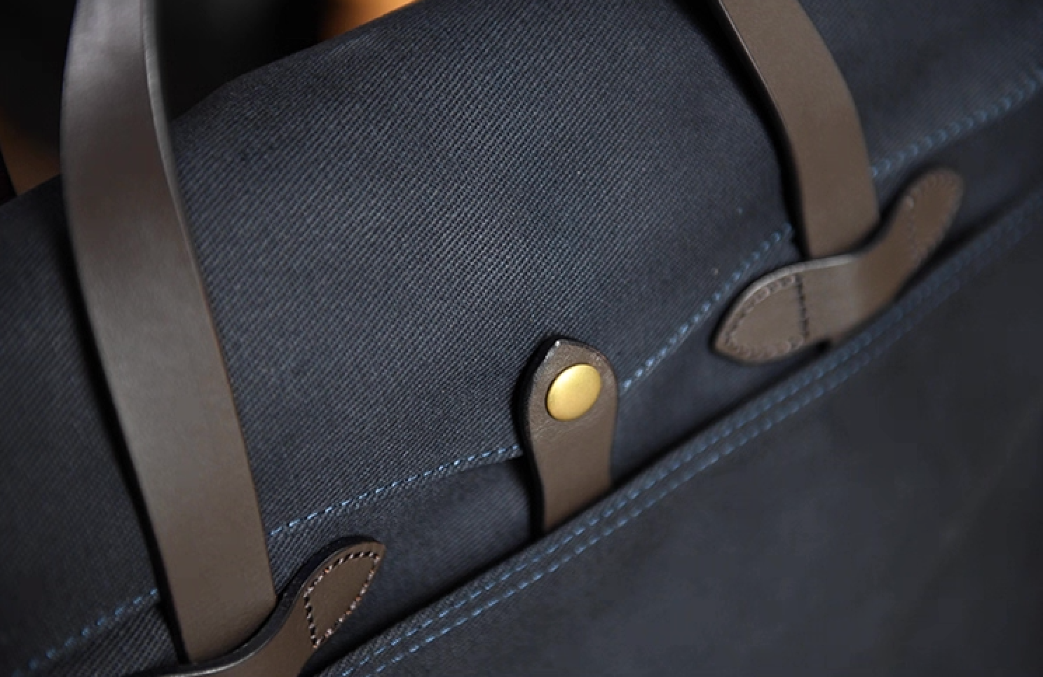 Close-up of navy waxed canvas briefcase showing brass snap button and leather strap details