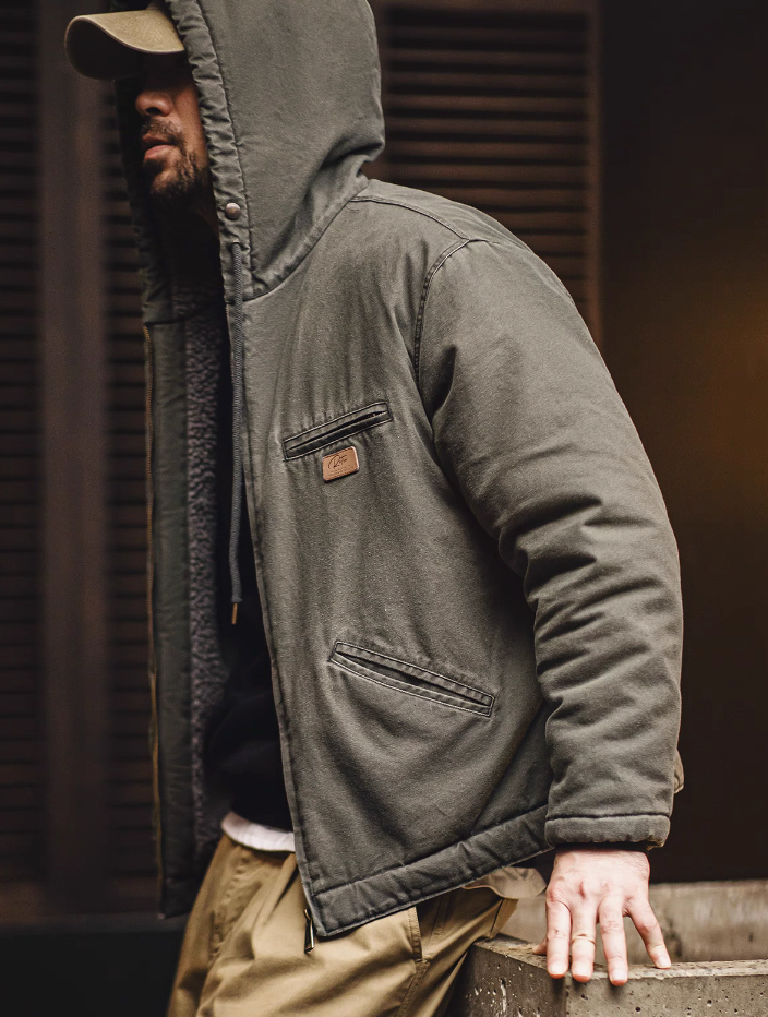 Man wearing dark green sherpa-lined hooded canvas jacket, side profile outdoors with hood up