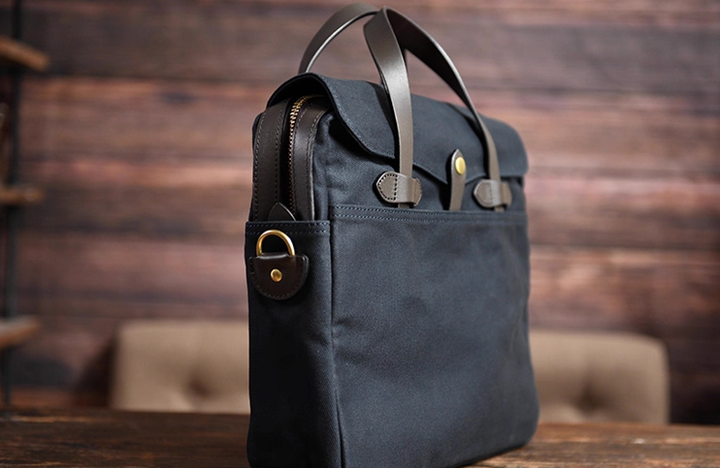 Side angle of navy waxed canvas laptop briefcase with leather handles and gold hardware