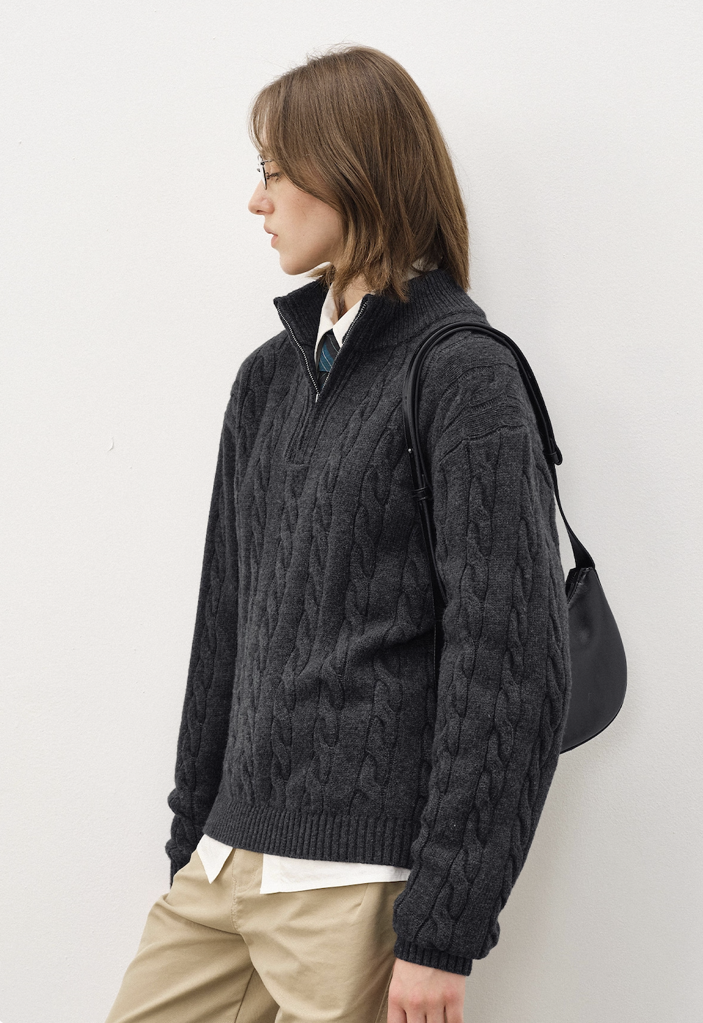 Side view of dark grey half-zip cable knit sweater with structured texture, styled with shoulder bag