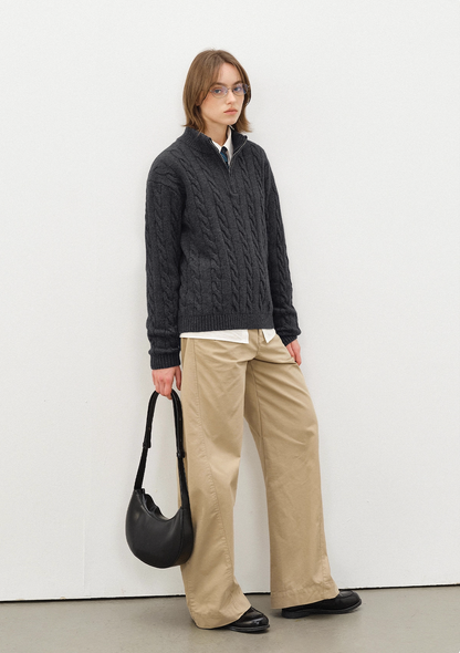 Full body look of model in dark grey half-zip cable knit sweater, beige wide-leg pants, black handbag