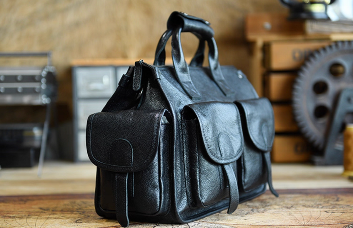 Side angle of black leather work and travel bag showing deep texture and multiple pockets