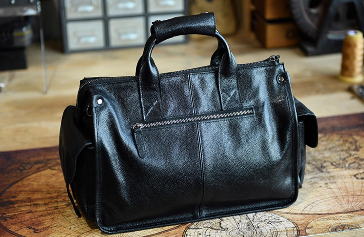 Back view of black leather duffle with zipper pocket and reinforced handle stitching