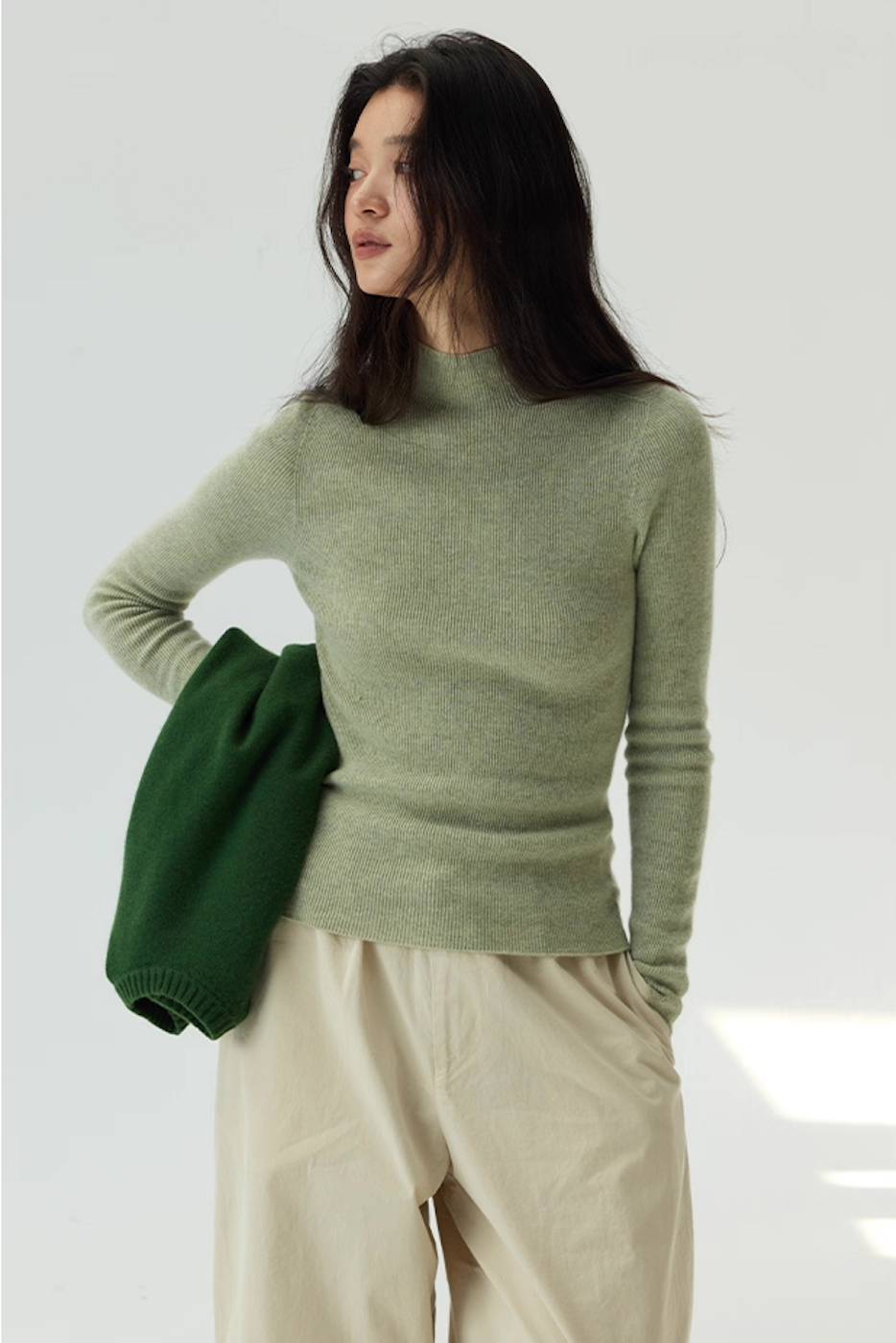 Model wearing light pink cashmere mock neck sweater with gray wide-leg pants and gray beanie, minimalist winter outfit