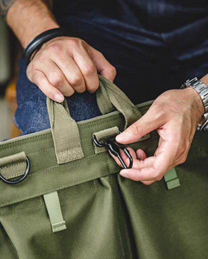 Close-up of army green canvas tote bag handle and front clip hardware detail with stitching and attachment points visible.