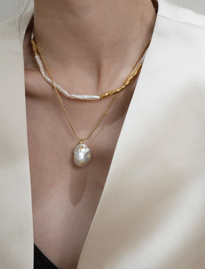 Model wearing baroque pearl gold accent choker necklace layered with gold chain and baroque pearl pendant over blazer outfit