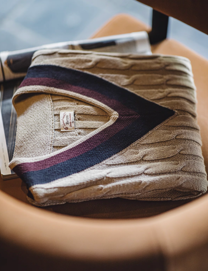 Folded cable knit khaki vest with navy and burgundy V-neck trim on chair