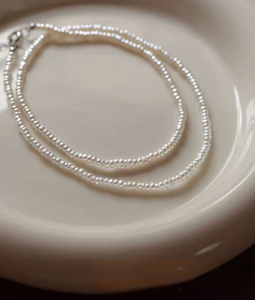 Classic pearl silver necklace styled as double layer flat lay on ceramic plate showing two strands of small freshwater pearls with silver clasp