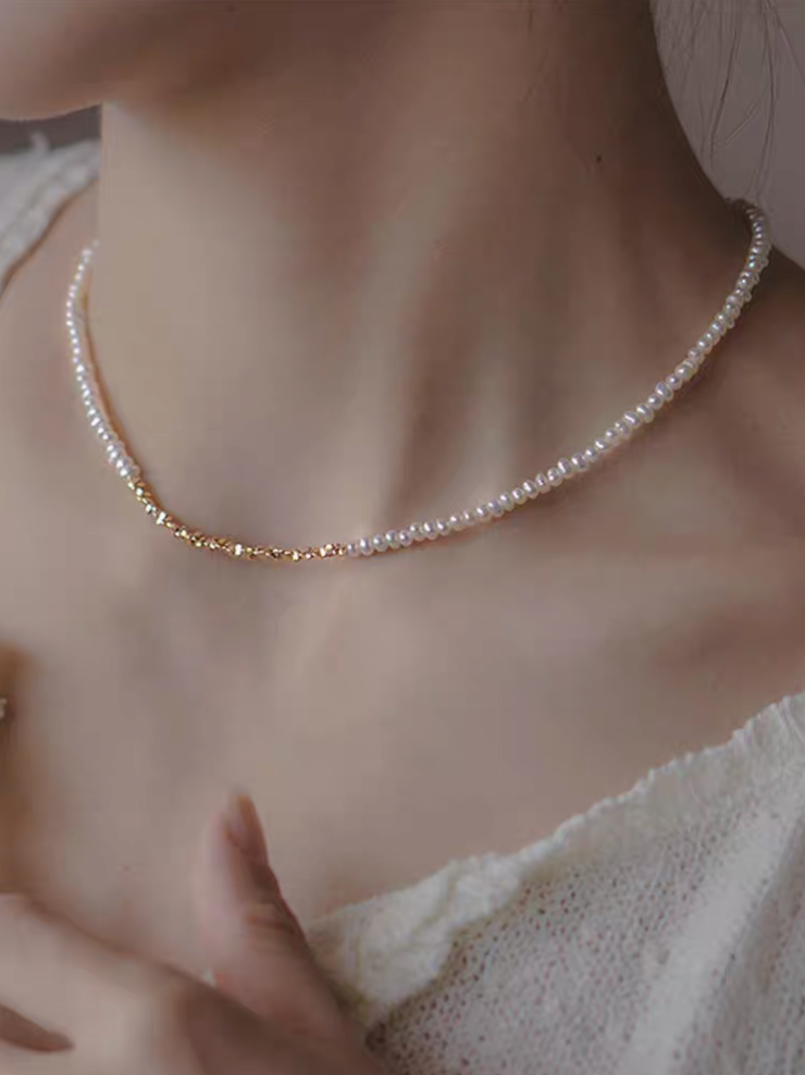 Model wearing delicate pearl strand necklace with gold-plated silver accents featuring natural freshwater pearls and gold fragments along neckline