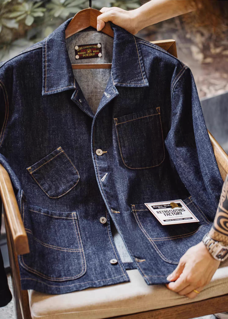 Denim work coat displayed on wooden chair showing heavyweight fabric texture