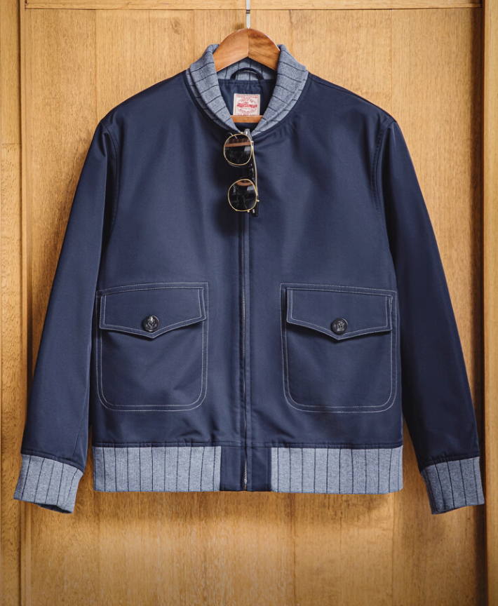 Navy bomber jacket hanging on wooden wall with sunglasses