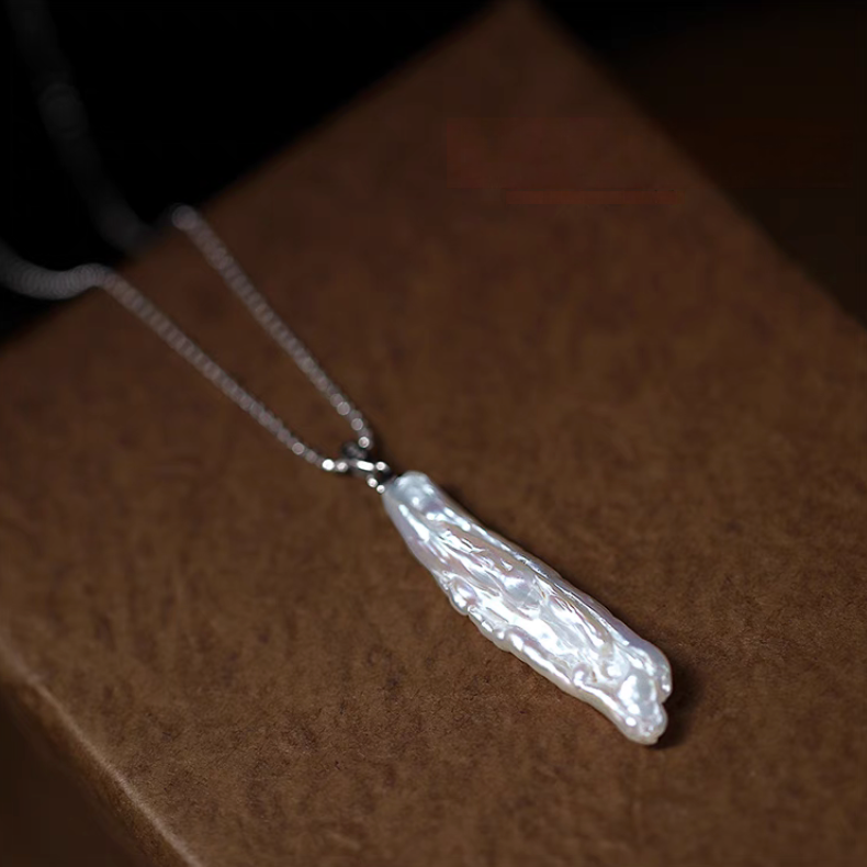 Close-up of organic baroque pearl drop necklace in silver on wooden surface highlighting elongated natural pearl pendant texture