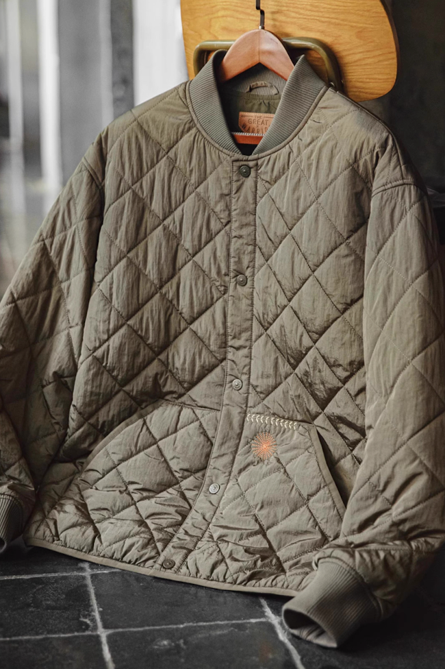Army green nylon quilted baseball jacket hanging on wooden hanger