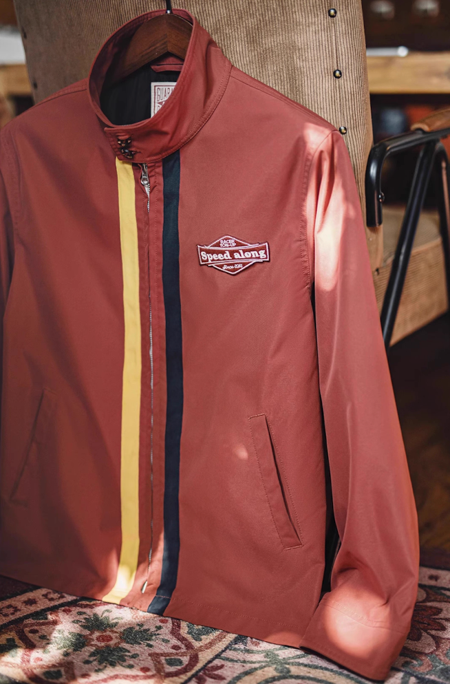 Brick red retro racing jacket hanging on chair, showing embroidered Speed Along patch